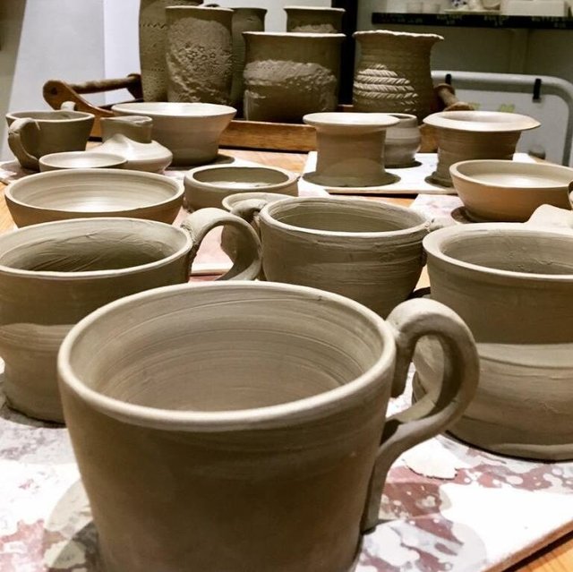 Close-up of unglazed clay mugs and pottery on a workbench.