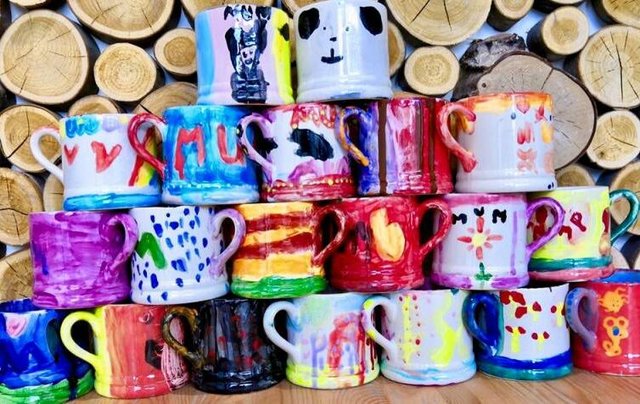 Colorful ceramic mugs with painted designs stacked against a log background.