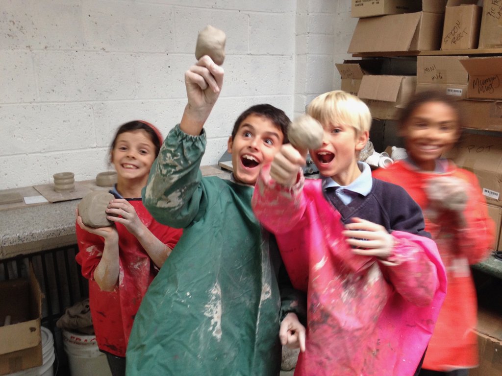 Four children holding clay figures, smiling and laughing in an art studio.
