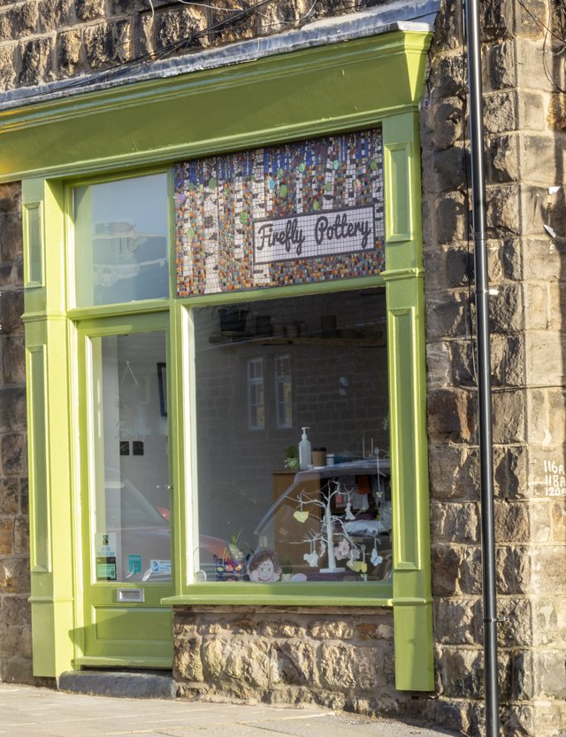 A green-framed storefront displays pottery and decorations. A mosaic sign reads