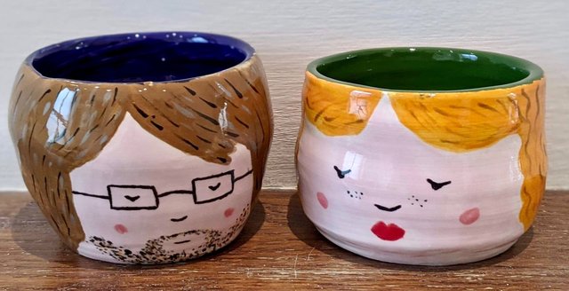 Two ceramic cups, one with a man's face and one with a woman's face.
