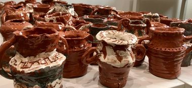 A collection of terracotta pottery vessels stacked on a white surface. The pots have textured surfaces and some are coated in white glaze.