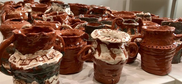 A collection of terracotta pottery vessels stacked on a white surface. The pots have textured surfaces and some are coated in white glaze.