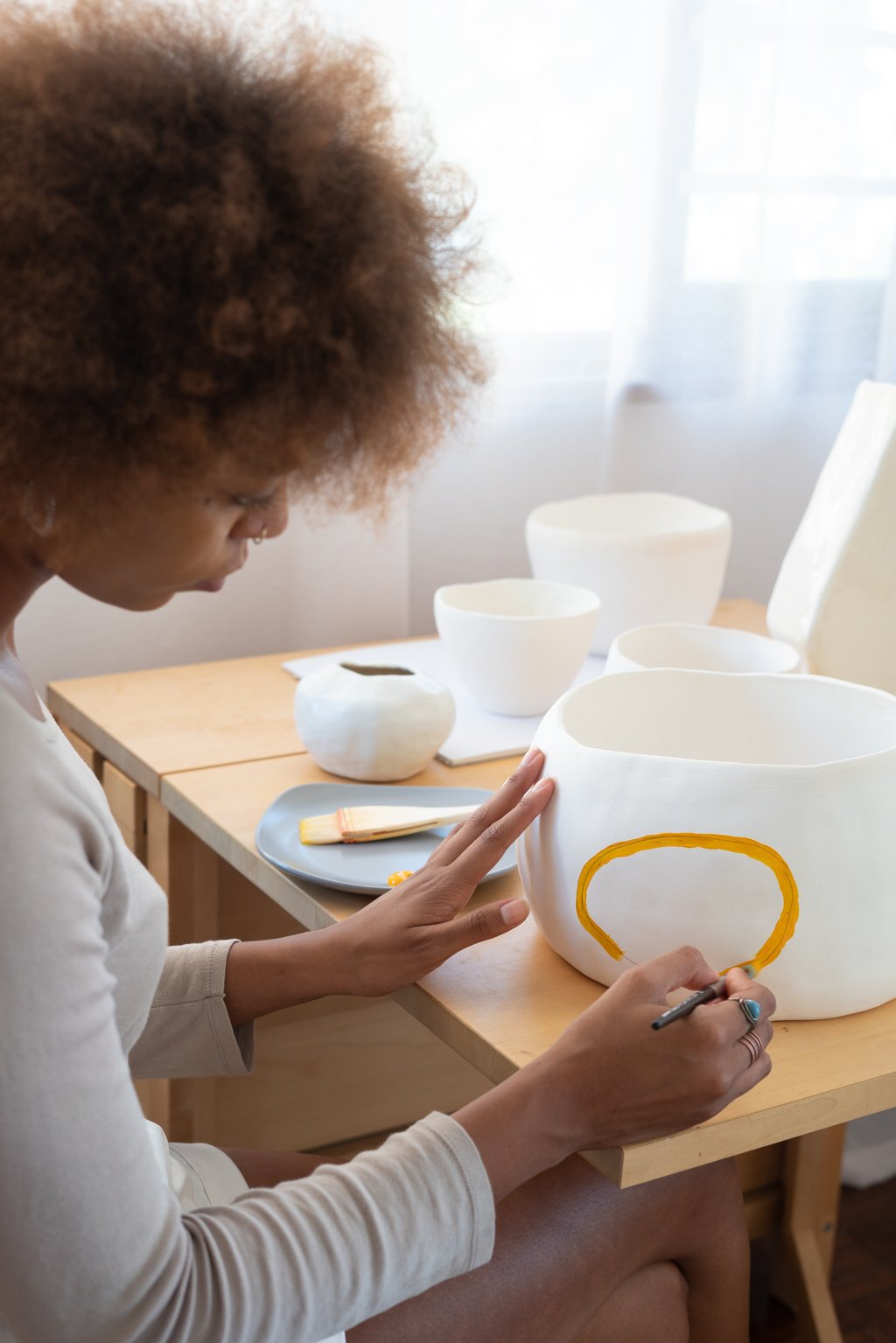 A person paints a ceramic bowl with a yellow line.