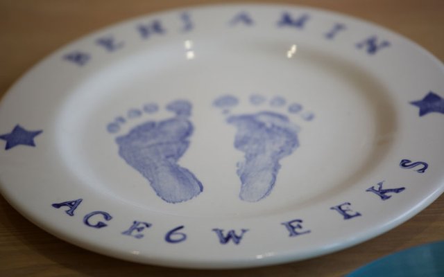 A white plate with blue ink footprints and the text '6 WEEKS' and a name around the rim.